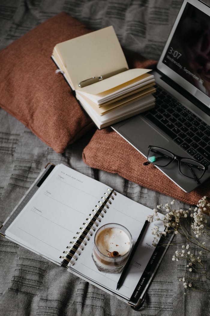 A warm, inviting home workspace featuring a notebook, laptop, and coffee on a soft surface.